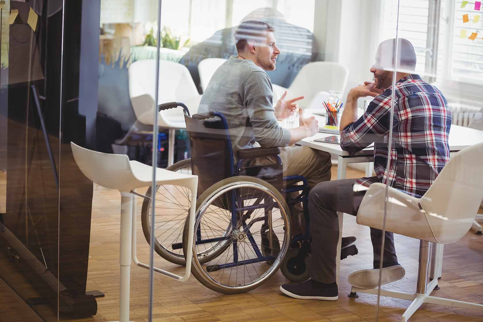 Man in a wheelchair talking to another man at a table in a conference room